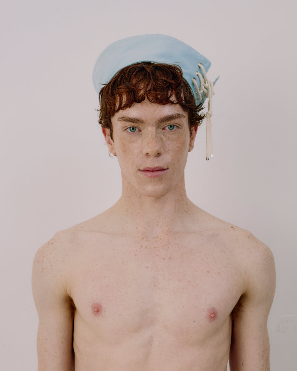 Person wearing a light blue cap with white strings on a plain background