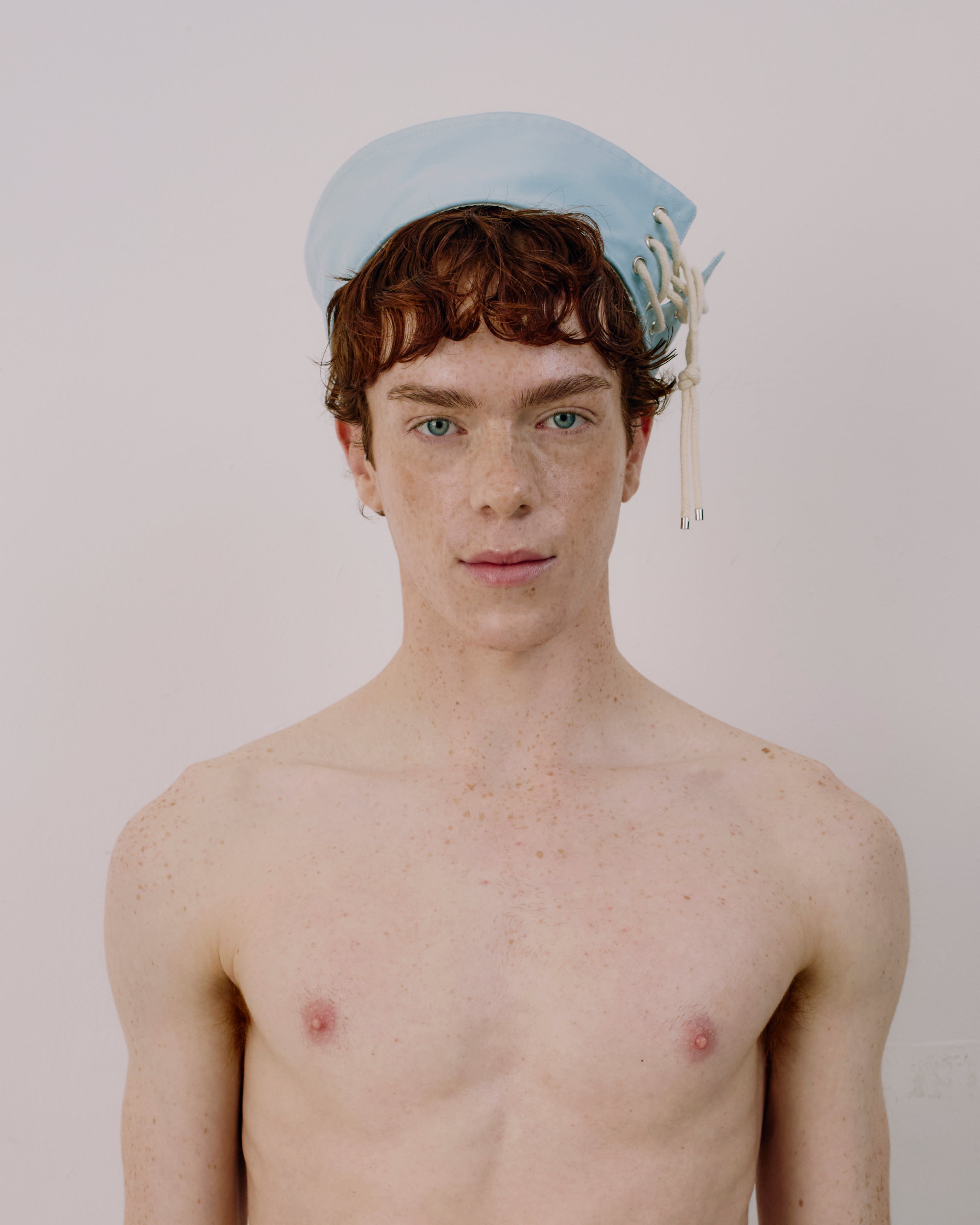 Person wearing a light blue cap with white strings on a plain background