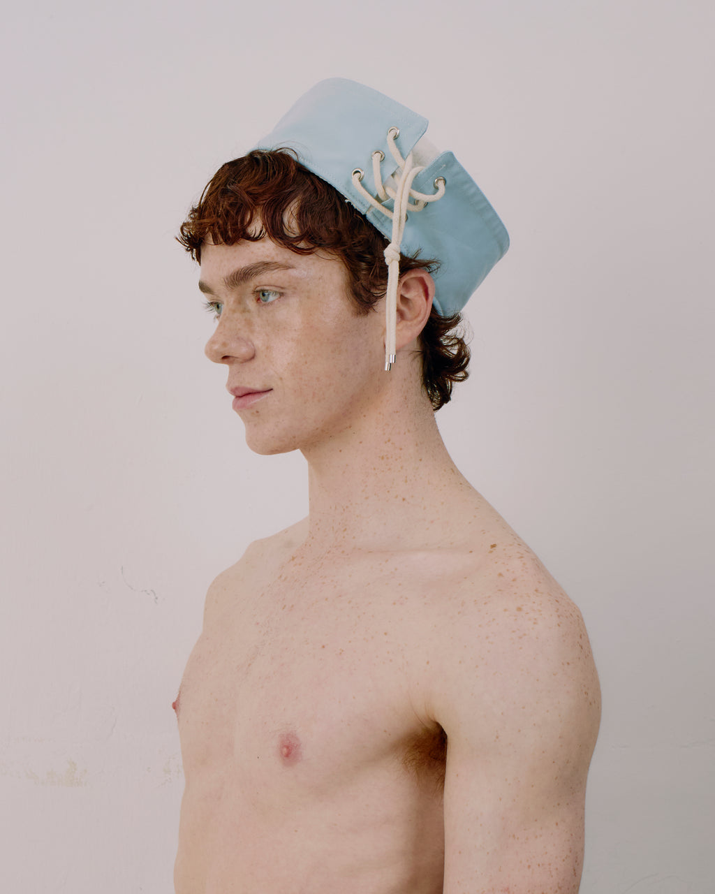 Person wearing a light blue cap with white strings on a plain background