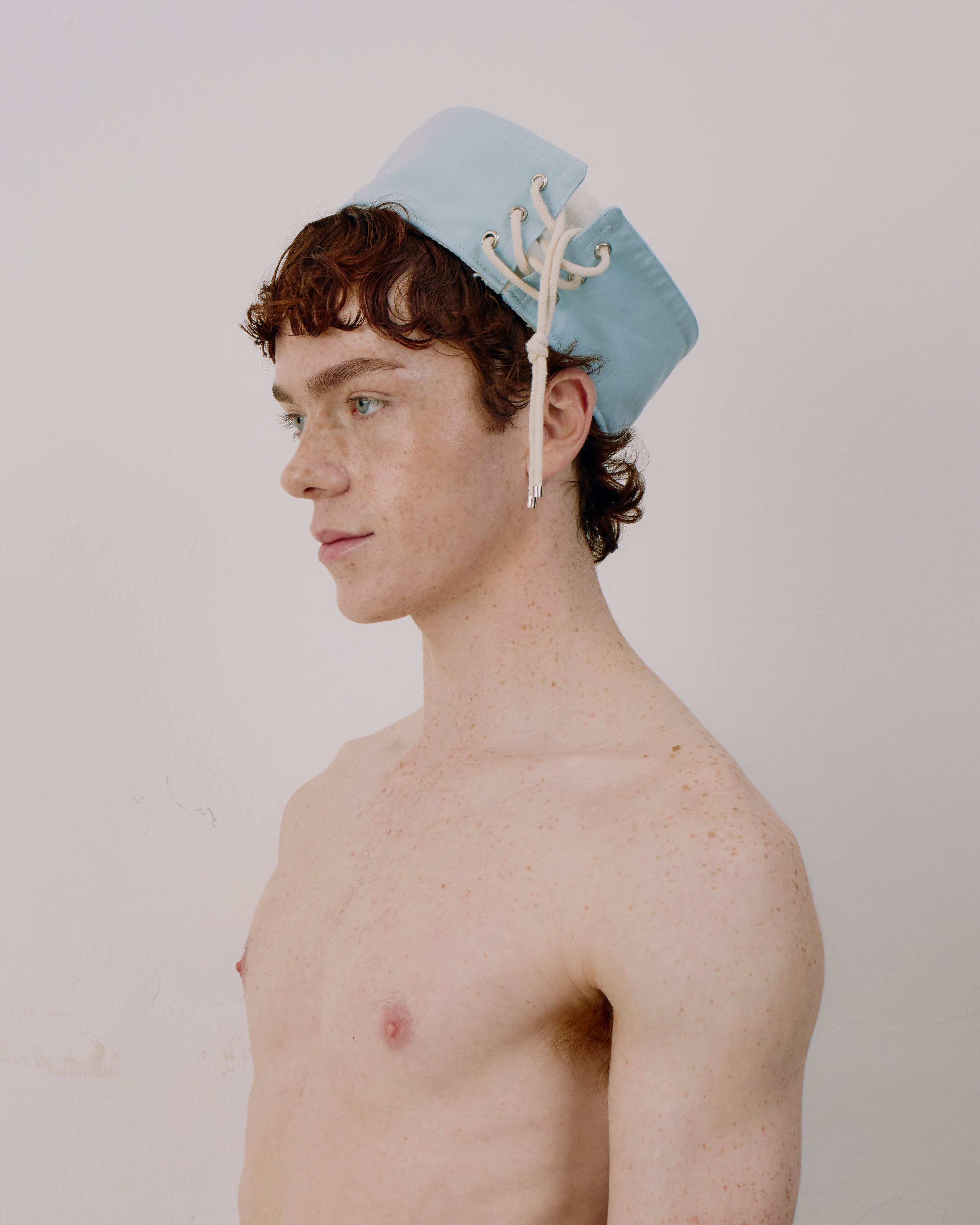 Person wearing a light blue cap with white strings on a plain background