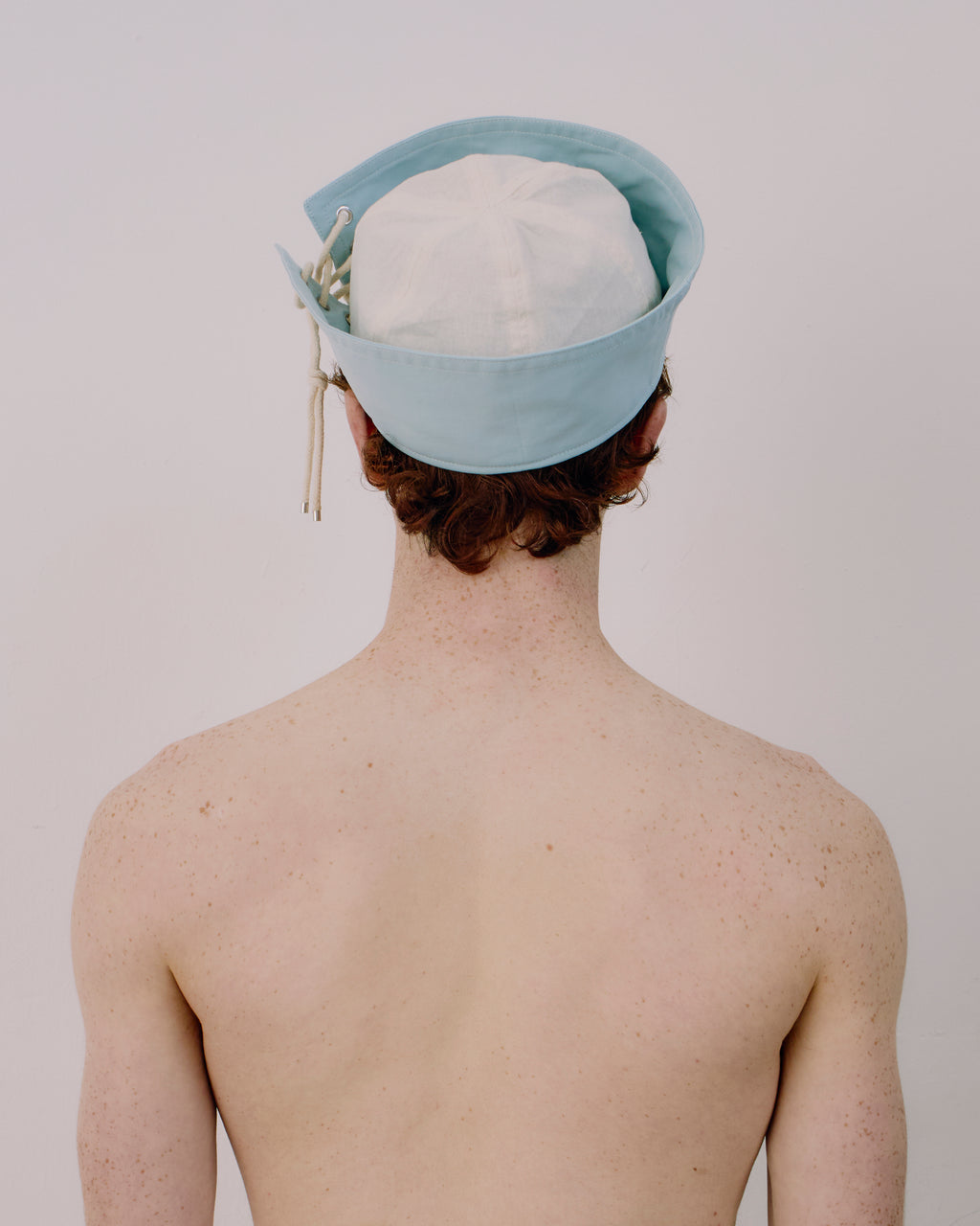 Person wearing a light blue cap with white strings on a plain background