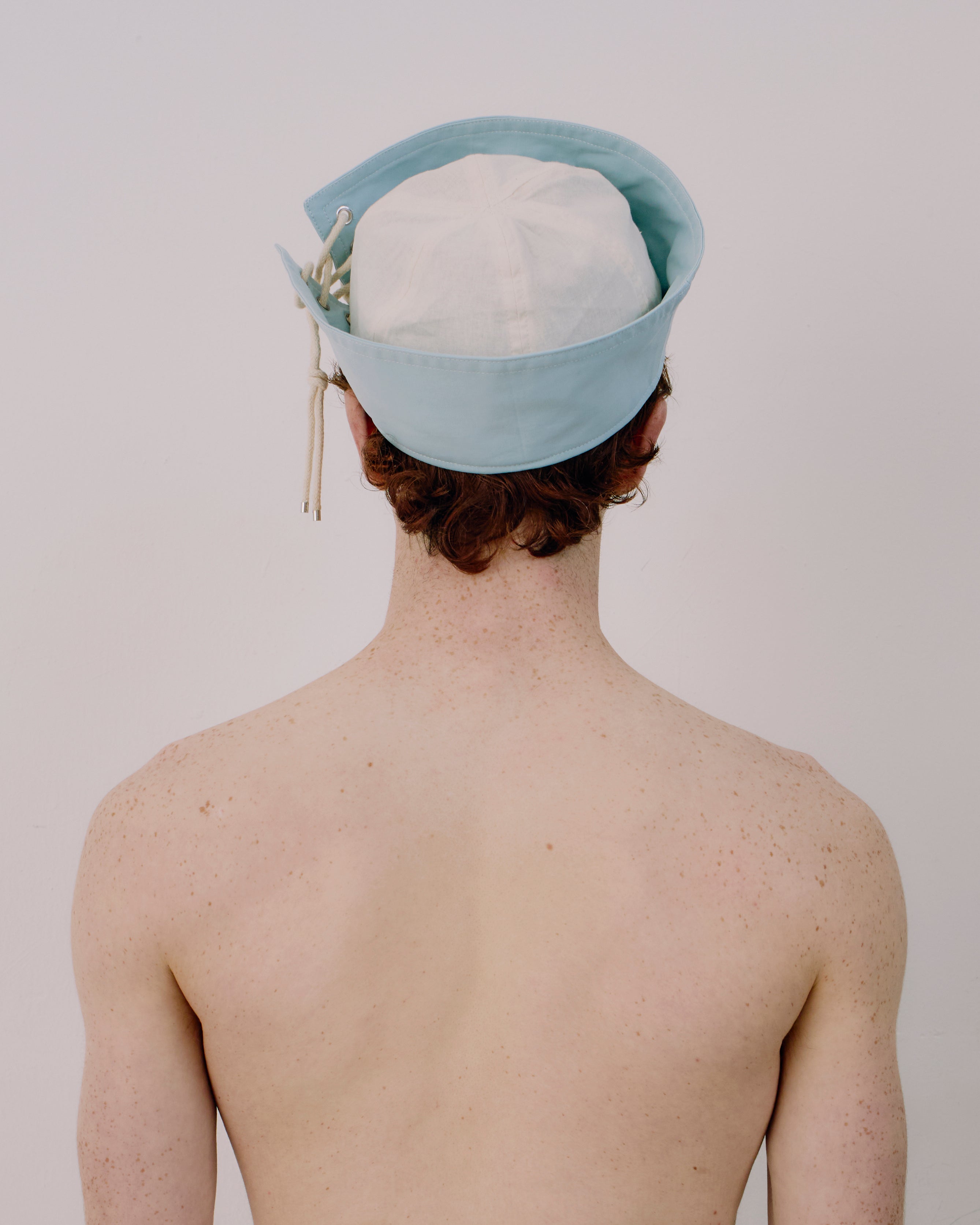 Person wearing a light blue cap with white strings on a plain background