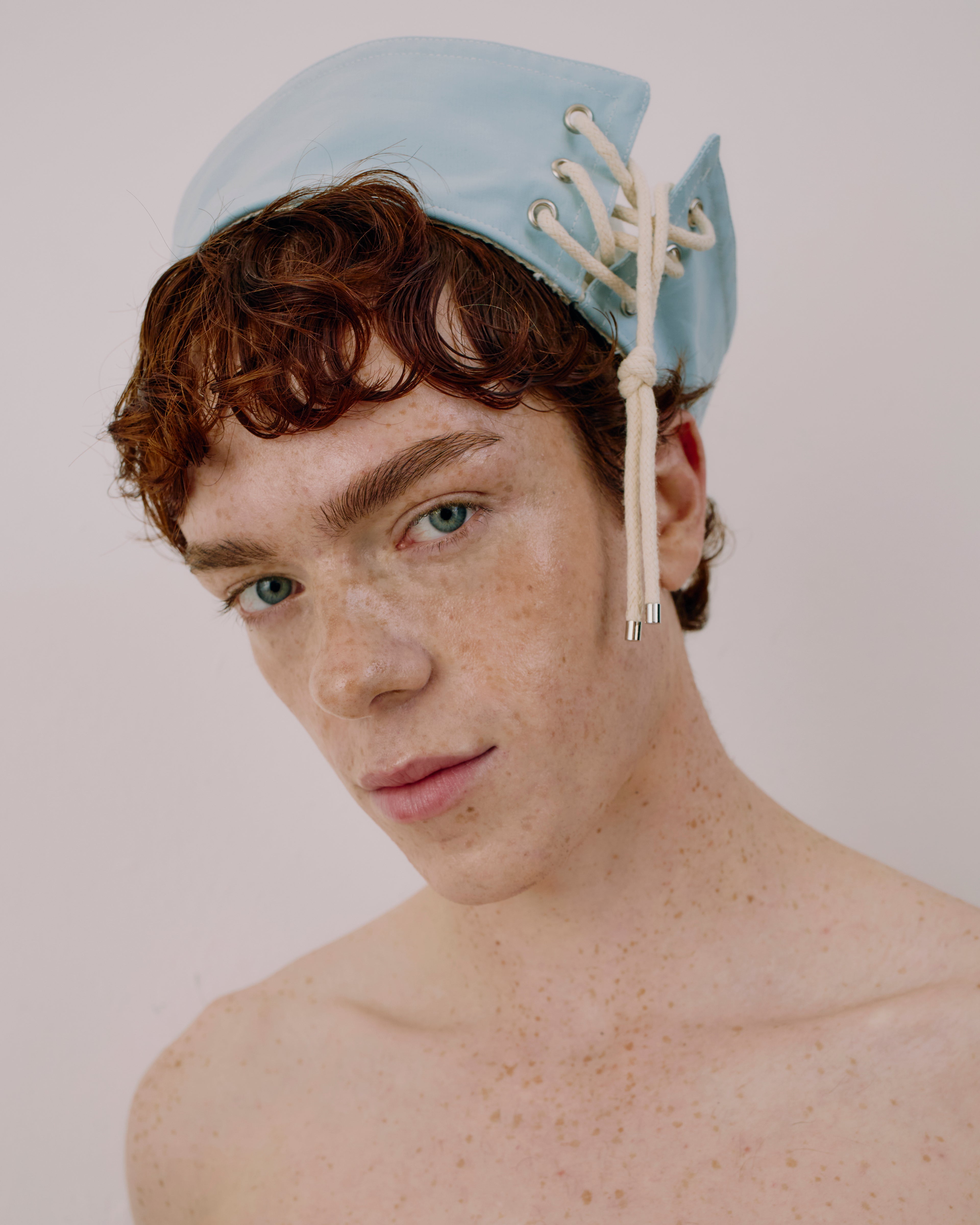 Person wearing a light blue cap with white strings on a plain background